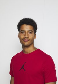 Rød bomulds T-shirt med et sort Jordan-logo på brystet. Korte ærmer og rund halsudskæring med en glat tekstur.