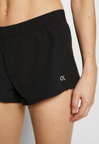 Shorts de sport noirs avec une taille élastique et un petit logo blanc sur le côté inférieur. Tissu doux avec une coupe décontractée.
