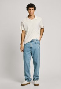Light beige polo shirt, relaxed-fit light blue jeans, white sneakers with brown soles. Simple design, soft texture, and casual style.