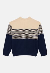 Strikkegenser med en kremfarget overdel og marineblå underdel. Har geometriske hvite mønstre over brystet og ermene.