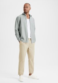 Lichtgroene overhemdd met een zak, gecombineerd met beige broek en witte sneakers. Glad stof en een ontspannen pasvorm.