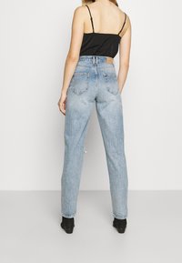 Jeans blu a vita alta con vestibilità rilassata, caratterizzati da un lavaggio sbiadito, tasche posteriori e orlo sfrangiato, abbinati a un top in camicia nero.