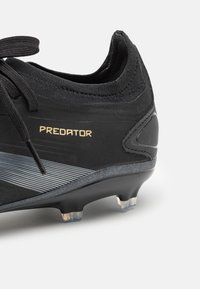 Zwarte voetbalschoenen met een gestructureerde bovenkant, gouden "PREDATOR" logo en grijze streep. Voorzien van gevormde noppen voor grip op grasoppervlakken.