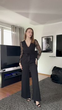 Čierny overal so zavinovacím dizajnom, priehľadnými rukávmi s bodkami a viazaním v páse. Má výstrih do V a siluetu so širokými nohavicami. Nastaviteľné ramienka.