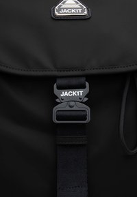 Zaino nero con una finitura liscia e opaca, dotato di una chiusura a fibbia prominente. Include un'etichetta triangolare con logo in argento e dettagli neri.