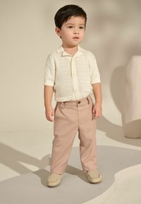 Helles cremefarbenes, gestricktes Kurzarmhemd mit Kragen, kombiniert mit hellrosa Hosen. Beige Mokassins runden das Outfit ab.