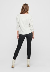 Witte gebreide trui, aangesloten zwarte jeans en crèmekleurige enkellaarsjes. De trui heeft lange mouwen en een losvallende pasvorm, met een lichte textuur.