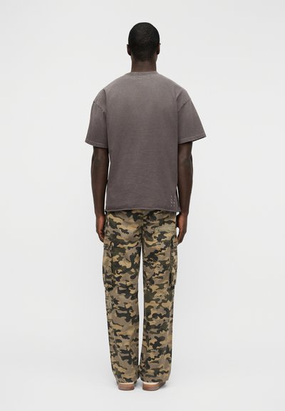 Γκρι κοντομάνικη μπλούζα και παντελόνι καμουφλάζ cargo. Το παντελόνι διαθέτει πολλαπλές τσέπες και άνετη εφαρμογή. Λείο υλικό και καθημερινός σχεδιασμός.