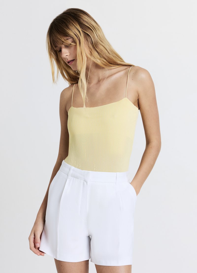 Top sans manches jaune à côtes avec un décolleté carré, associé à un short blanc taille haute avec des plis frontaux et des poches latérales.