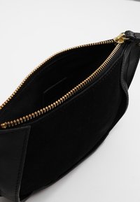 Černá taštička vyrobená z nubuku se zlatým zipem. Interiér je podšitý a ukazuje jednoduchý, elegantní design bez dalších ozdob.