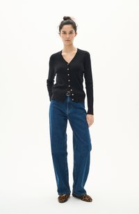 Svart ribbad kofta med V-hals, guldknappar, kombinerad med högmidjade blå vida jeans och leopardmönstrade slip-on skor.