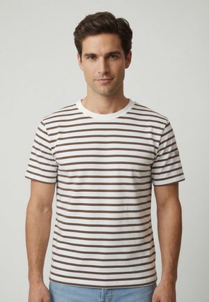 Uomo che indossa una maglietta bianca a maniche corte con sottili righe orizzontali marroni, in piedi davanti a uno sfondo grigio chiaro uniforme.