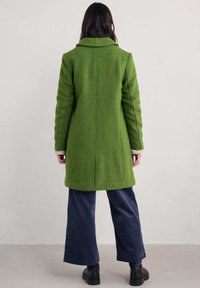 Grön texturerad kappa med bred krage, långa ärmar och rak skärning. Tillsammans med marinblå kordbyxor och svarta ankelstövlar.