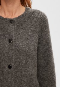 Grå tröja med raglanärmar, texturerad tyg, rundad halsringning och fem svarta knappar framtill. Mjuk och något fuzzy textur.
