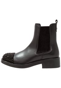 Bottine en cuir noir avec un panneau élastique texturé noir. L'orteil est orné de clous noirs et d'un talon carré.
