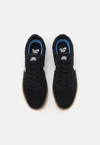 Zapatillas de ante negro con un logo en forma de swoosh blanco. Presentan una suela de goma, cordones negros y acentos azules en el interior del cuello.