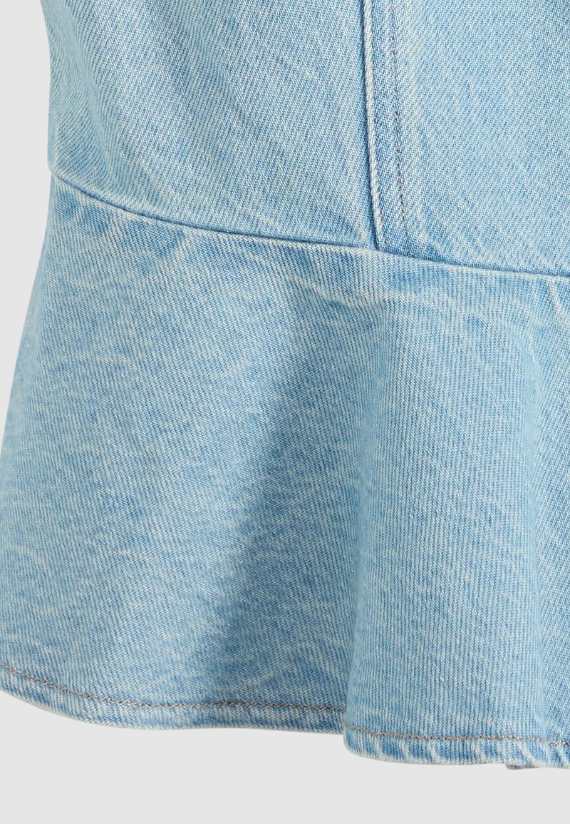 Lichtblauwe denimstof met zichtbare stiksels en een wijde naaddetail aan de onderrand van een kledingstuk.