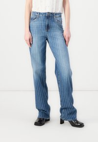 Jean en denim bleu clair avec des rayures verticales blanches, un design classique à cinq poches et une silhouette légèrement évasée.