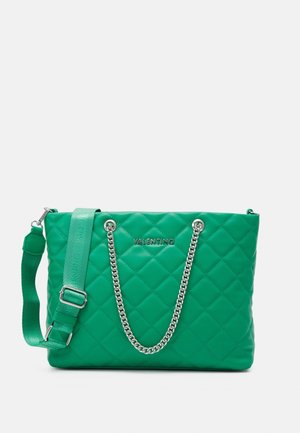 Groene gewatteerde leren tote bag met zilveren kettingaccenten, een afneembare strap en gegraveerde branding aan de voorkant.