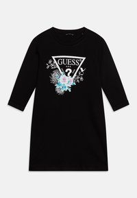 Musta pitkähiha-mekko, jossa on valkoinen kolmionmuotoinen "GUESS"-logo sinisin ja vaaleanpunaisin kukkakuvioin. Pehmeää puuvillamateriaalia, rento istuvuus.