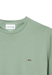 T-shirt vert clair en 100 % coton pima, avec un col rond côtelé et un petit logo crocodile brodé sur la poitrine gauche.