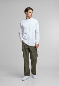 Camisa blanca de manga larga con cuello alto, combinada con pantalones cargo verde oliva y zapatillas blancas. El conjunto tiene un corte relajado.