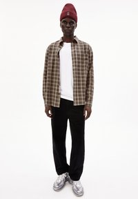 Geruite flanellen shirt in aardetinten over een wit T-shirt, gecombineerd met zwarte corduroypantalon en grijze sneakers, afgewerkt met een rode gebreide muts.