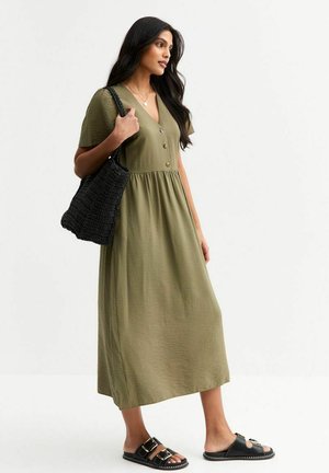 Olive green midi dress with short sleeves, button detailing, and a gathered waist. Worn with a black woven tote and black slide sandals.