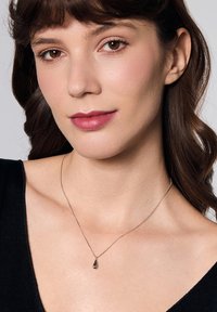 Srebrny naszyjnik z czarnym pendansem w kształcie kropli. Modelka nosi czarną bluzkę, eksponując naszyjnik na swojej skórze.