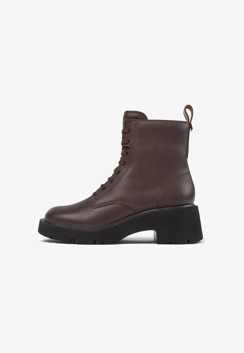 Bota de tobillo marrón con cordones y suela gruesa negra, con una pequeña lengüeta en la parte trasera, contra un fondo blanco.