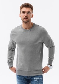 Grijze sweatshirt met een ronde hals, geribbelde boorden en zoom. Gemaakt van zachte stof met een gladde textuur, gecombineerd met versleten blauwe jeans.