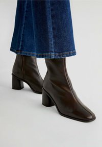 Brown leather ankle boots with a square toe, zip closure, and chunky, round heel. Paired with wide-leg blue jeans, showing hem details.
