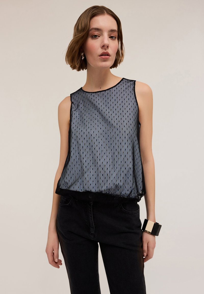 Mouwloos topje van doorzichtig donkerblauwe stof met verticale streepjes. Heeft een losse pasvorm en een zwarte zoom. Gecombineerd met zwarte denim broek.