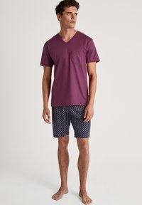 Bordeauxfarbenes V-Ausschnitt-T-Shirt mit Tasche, kombiniert mit navy-blauen gemusterten Shorts mit geometrischem Design. Leichtes Material, lässige Passform.