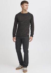 Mørk, teksturert langermet skjorte med rund hals og raglan-langermer, kombinert med mørkfargede bukser og grå sneakers.