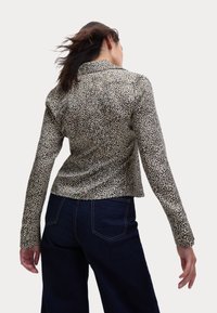 Camisa de manga larga estampada en beige y negro con un diseño ajustado y cuello tipo camisa, que presenta un sutil patrón de animales y puños con botones.