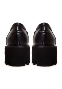 Paire de mocassins en cuir noir avec semelles en caoutchouc épaisses et robustes, vue de dos sur fond blanc.