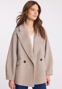 Beżowy płaszcz wełniany z podwójnym zapięciem, z dużymi klapami, dwoma bocznymi kieszeniami i czarnymi guzikami, o teksturowanej tkaninie, luźnym kroju.