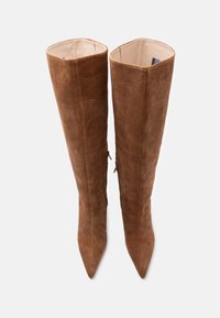 Smeđe brušene kožne čizme do koljena s vrhovima u obliku špice i suptilnim reljefnim uzorkom, prikazane uspravno na jednobojnoj svijetloj pozadini.