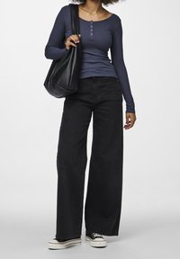 Marineblå ribbad långärmad topp med knappdetaljer, kombinerad med vida svarta jeans och en svart tote-väska, kompletterad med svart och vita sneakers.