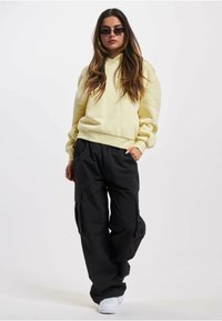 Un hoodie jaune à coupe décontractée avec des poignets en côtelé, assorti à un pantalon cargo noir avec des poches latérales et des baskets blanches.