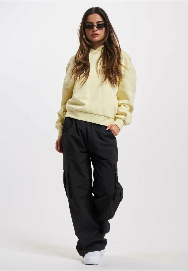Un hoodie jaune à coupe décontractée avec des poignets en côtelé, assorti à un pantalon cargo noir avec des poches latérales et des baskets blanches.