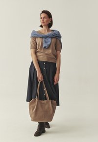 Haut en maille marron, pull bleu drapé, jupe en denim foncé avec boutons dorés, sac à main en suède beige, bottes marron. Design et couleurs minimalistes.
