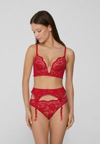 Rotes Spitzenunterwäsche-Set mit tiefem V-Ausschnitt-Bralette und Strumpfhalter mit Ausschnitten, Rüschen und satinartigen Akzenten. Detailliertes florales Muster sichtbar.