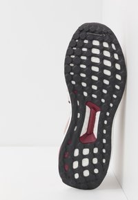 Semelle de chaussure en caoutchouc noir avec des motifs circulaires, présentant une touche rouge et une semelle intermédiaire blanche. Forme profilée pour une adhérence et une flexibilité optimales.