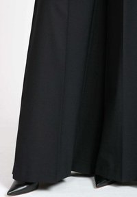 Pantaloni neri a gamba larga realizzati in un tessuto liscio, che presentano una silhouette pulita e pieghe ben definite. Abbinati a tacchi a punta neri.