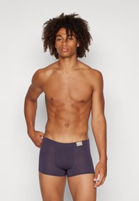 Männer Boxer-Shorts aus dunkellila Stoff mit glatter Textur, elastischem Bund und einem kleinen, neutralen Logoetikett auf der Vorderseite.