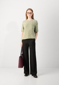 Light green textured knit top with short sleeves, paired with black wide-leg trousers. Model holds a burgundy bag with dark accents.