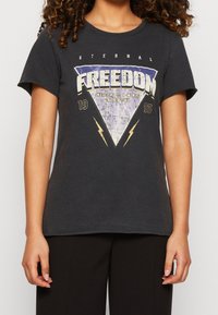 Camiseta de algodón negra con un gráfico vintage que lleva la palabra "LIBERTAD", rodeada de un triángulo y motivos de rayos. Mangas cortas.