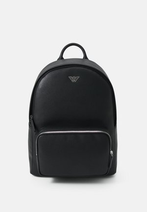 Zaino in pelle nera con design arrotondato, tasca anteriore con zip, accessori in argento e un logo ben visibile sulla parte anteriore.